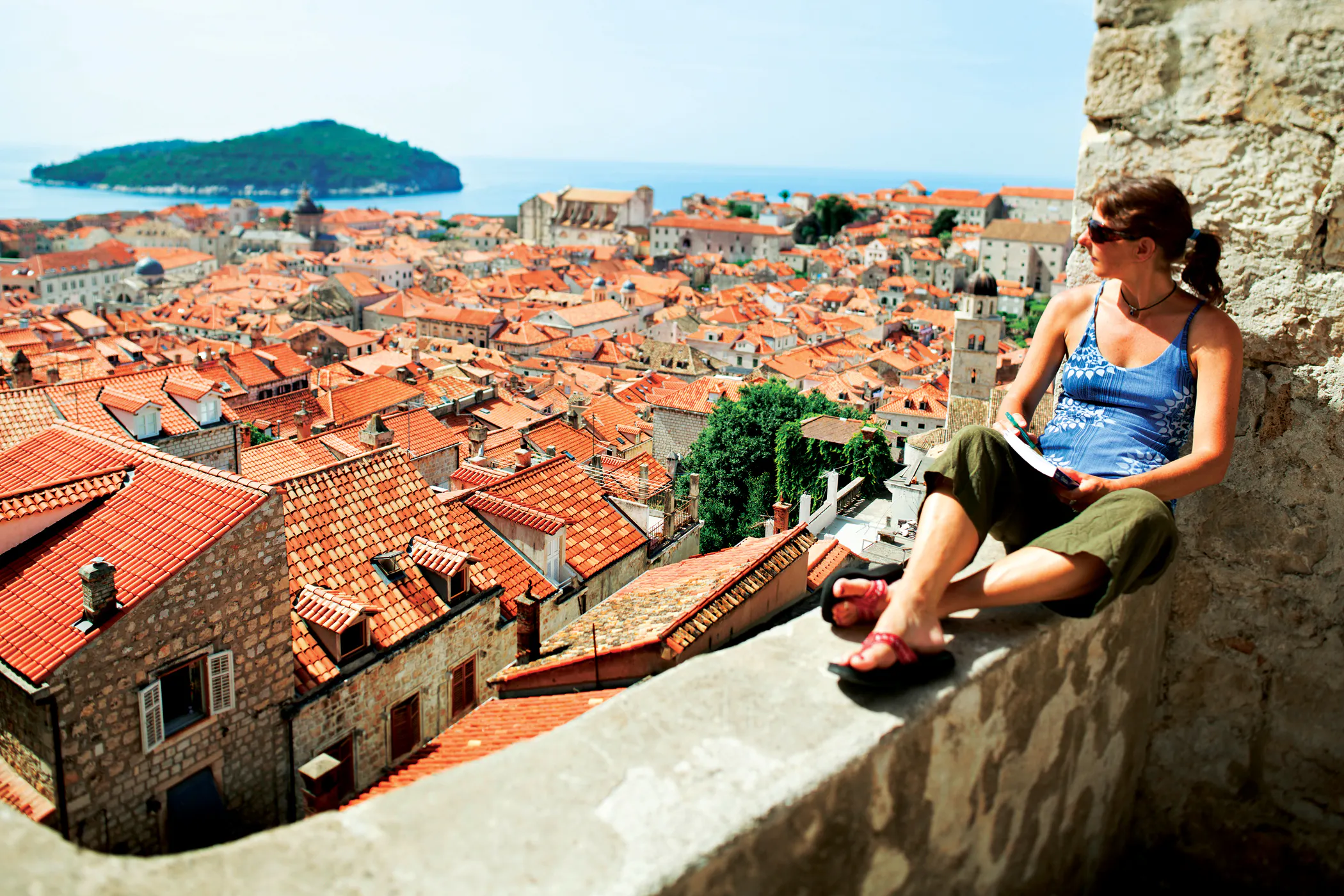 Woman traveler on the city wall looking out over the ancient city of Dubrovnik, reading and writing postcards, Croatia