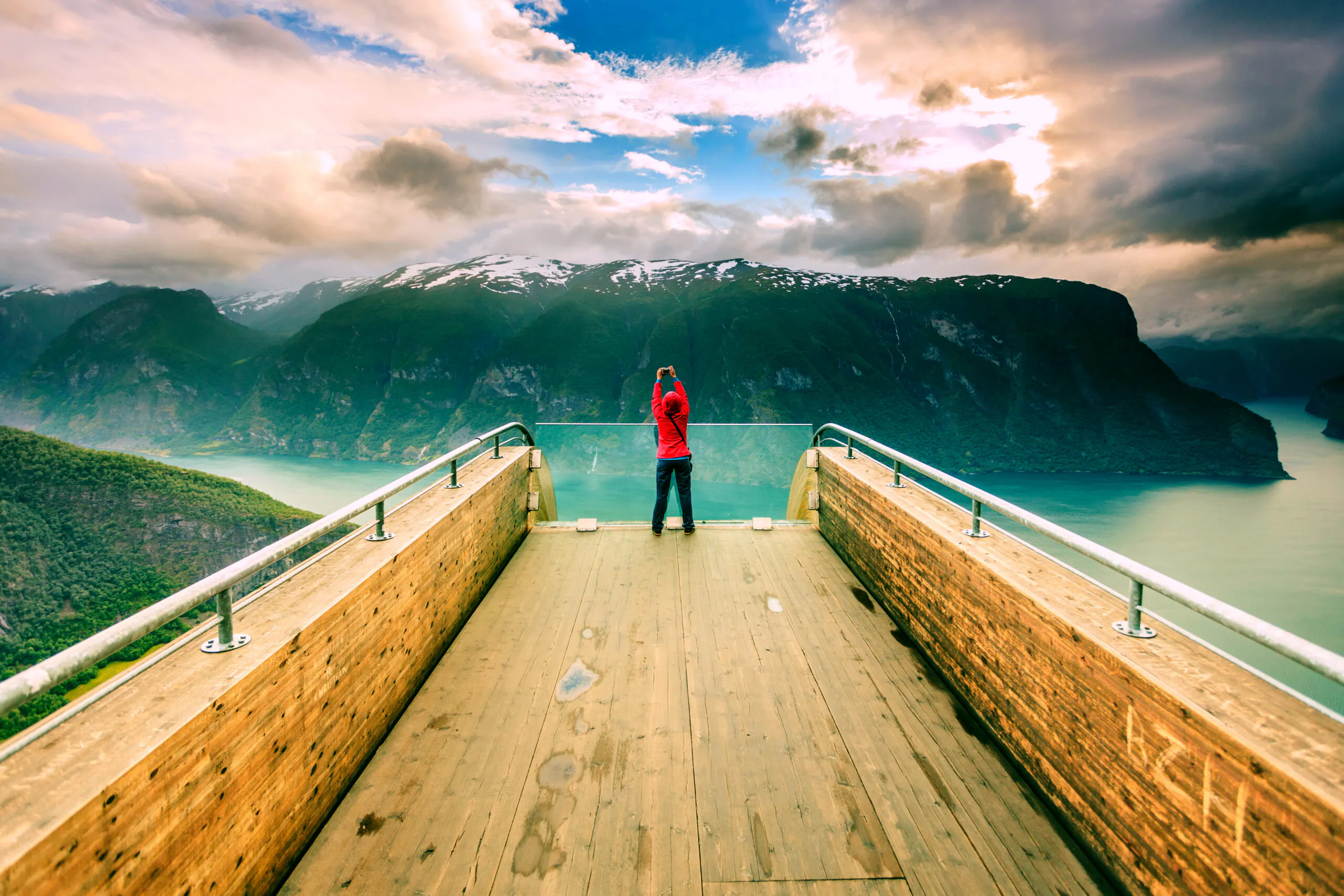 Woman tourist nature photographer taking photo with camera, enjoying Aurland fjord landscape from Stegastein lookout, Norway Scandinavia.