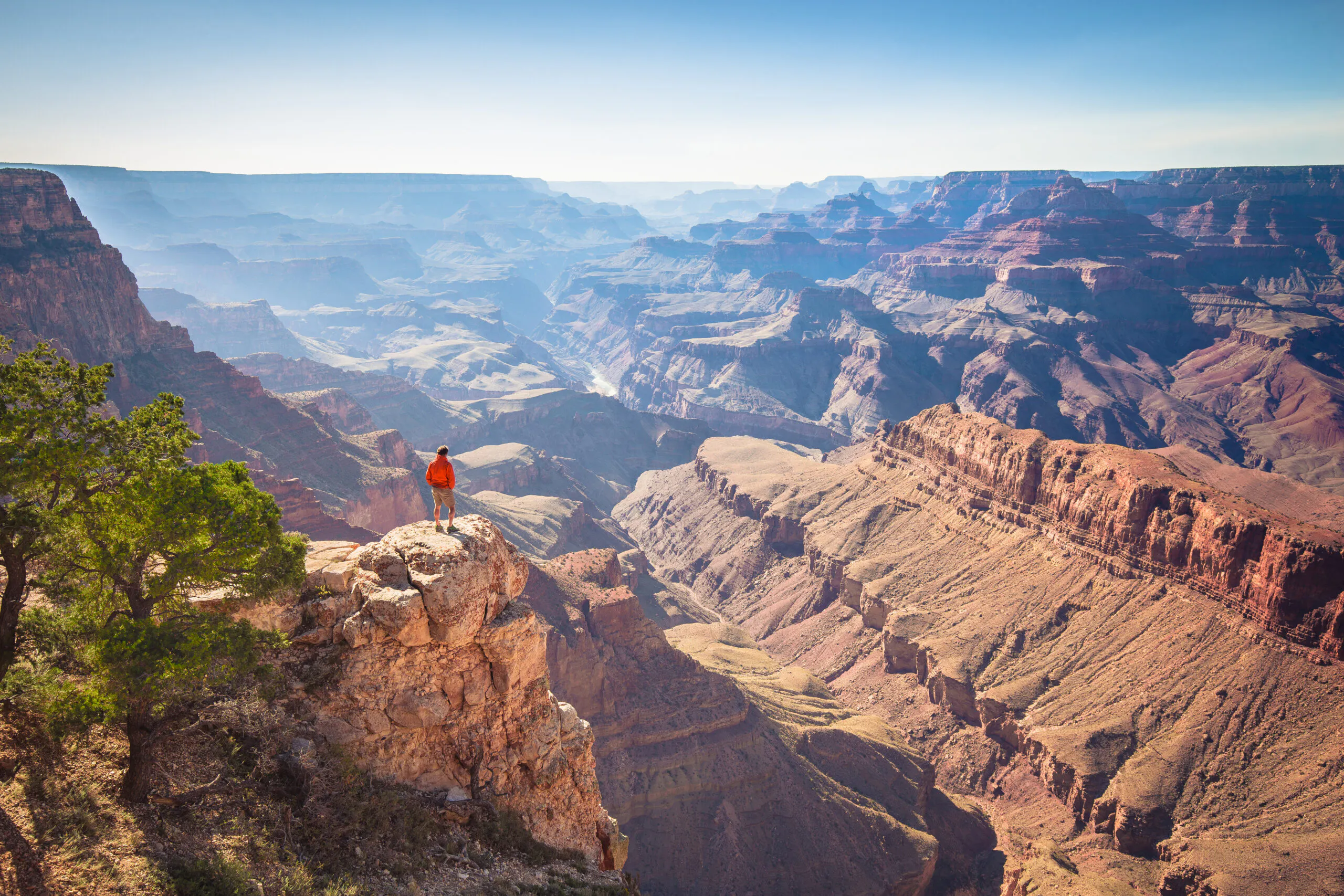 A male hiker is standing on a steep cliff taking in the amazing view over famous Grand Canyon on a beautiful sunny day with blue sky in summer Grand Canyon National Park Arizona USA