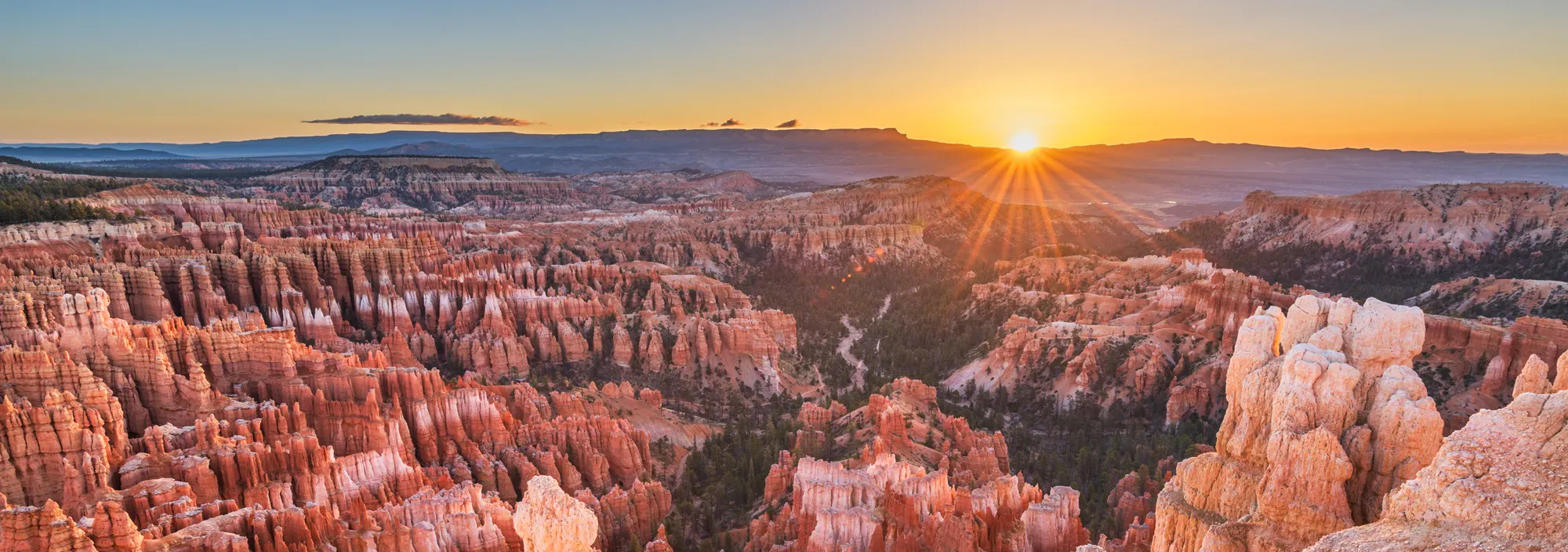 Sunrise over Bryce Canyon National Park, one of Utah national parks, reveals rugged red rock formations, hoodoos, and a wide, clear sky—perfect for unforgettable hiking adventures.