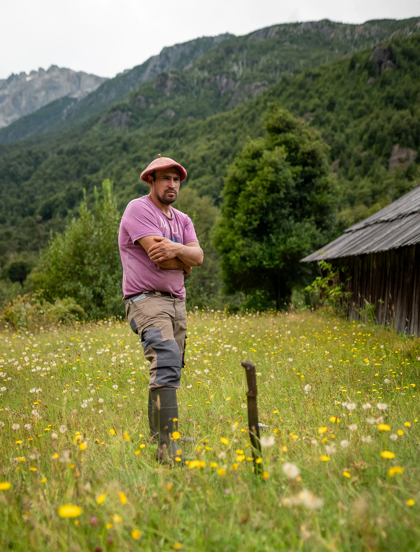 A Chilean man standing in a meadow in Cochamo Valley with forested peaks behind him