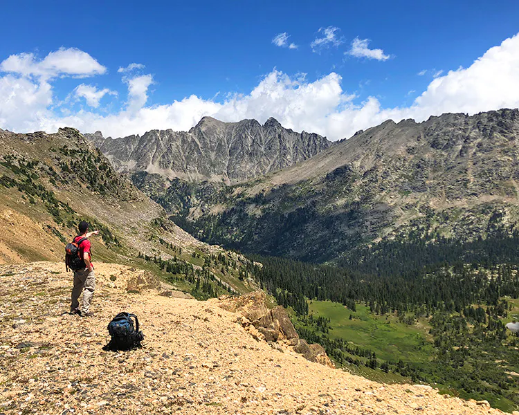 Hiker above treeline in Rocky Mountain National Park pointing at a deep river valley