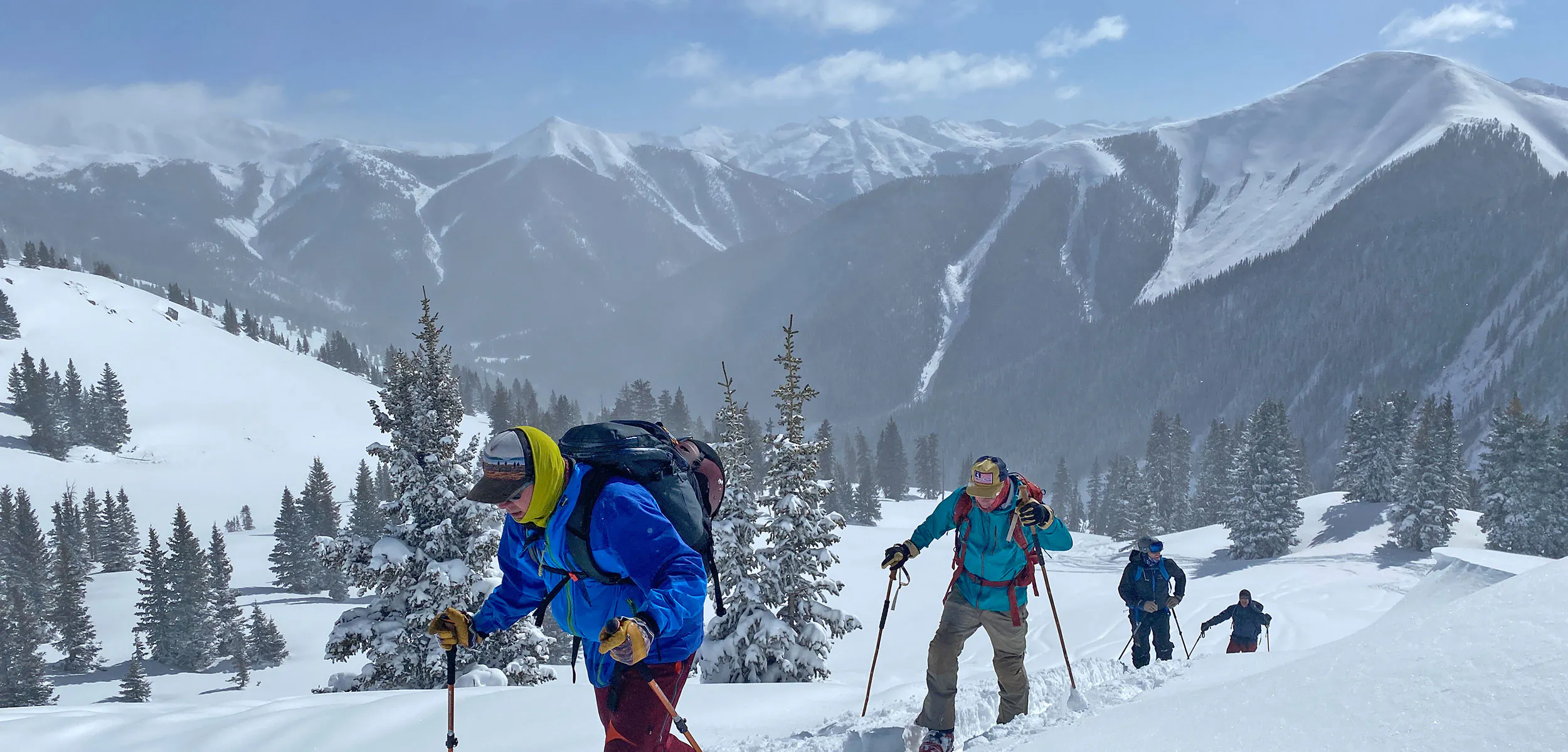 A group of backcountry skiers breaking trail in the Rocky Mountains of Colorado with alpine peaks, ridges and basins in the background