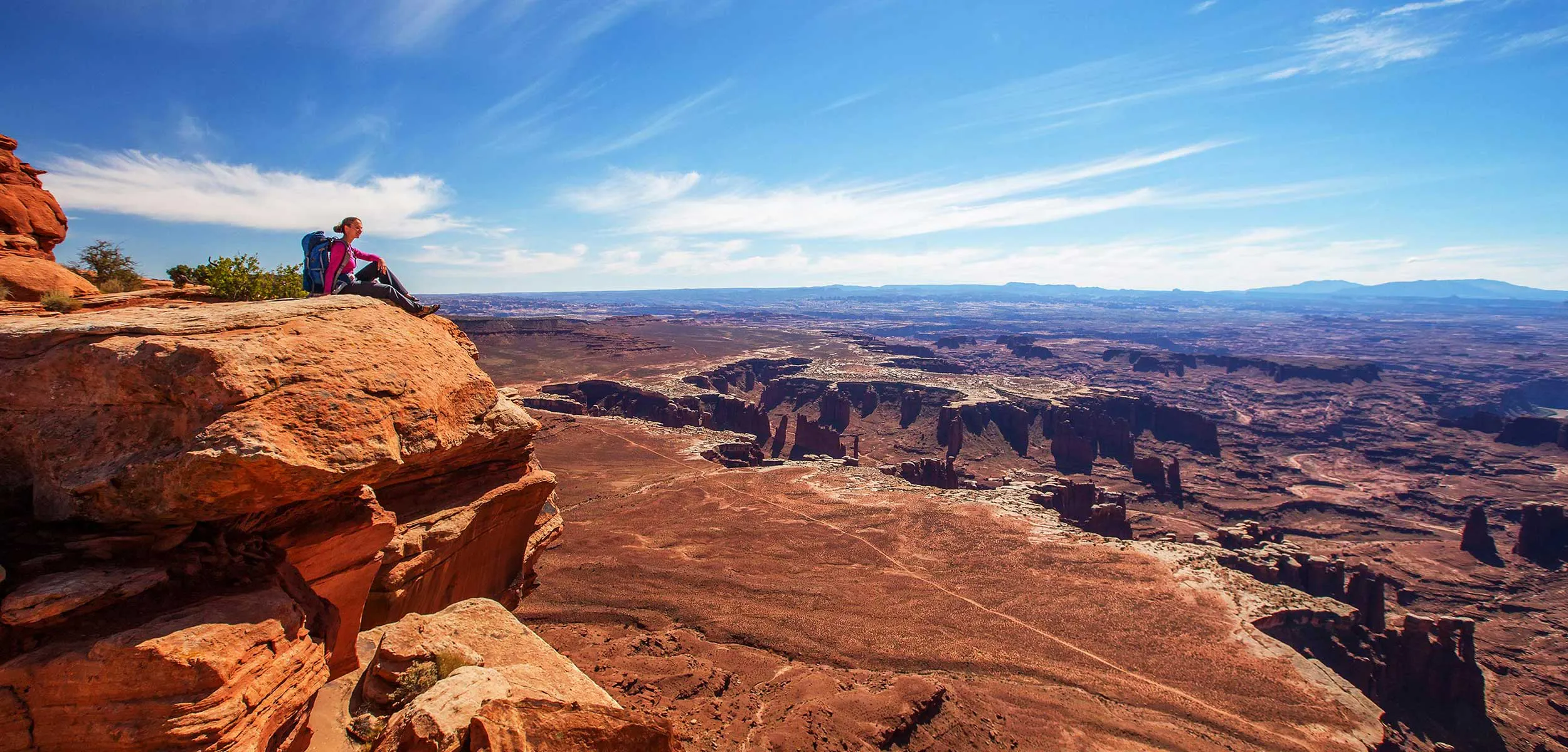 Woman sitting on a sandstone boulder over looking the Maze of Canyonlands National Park
