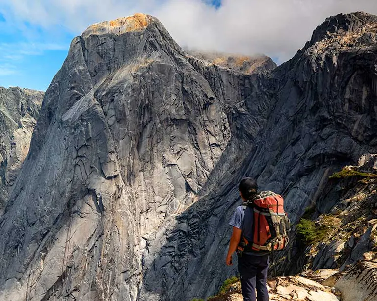 Hiker with a red backpack standing and looking out at a 3,000 foot cliff in Cochamo Valley, Patagonia
