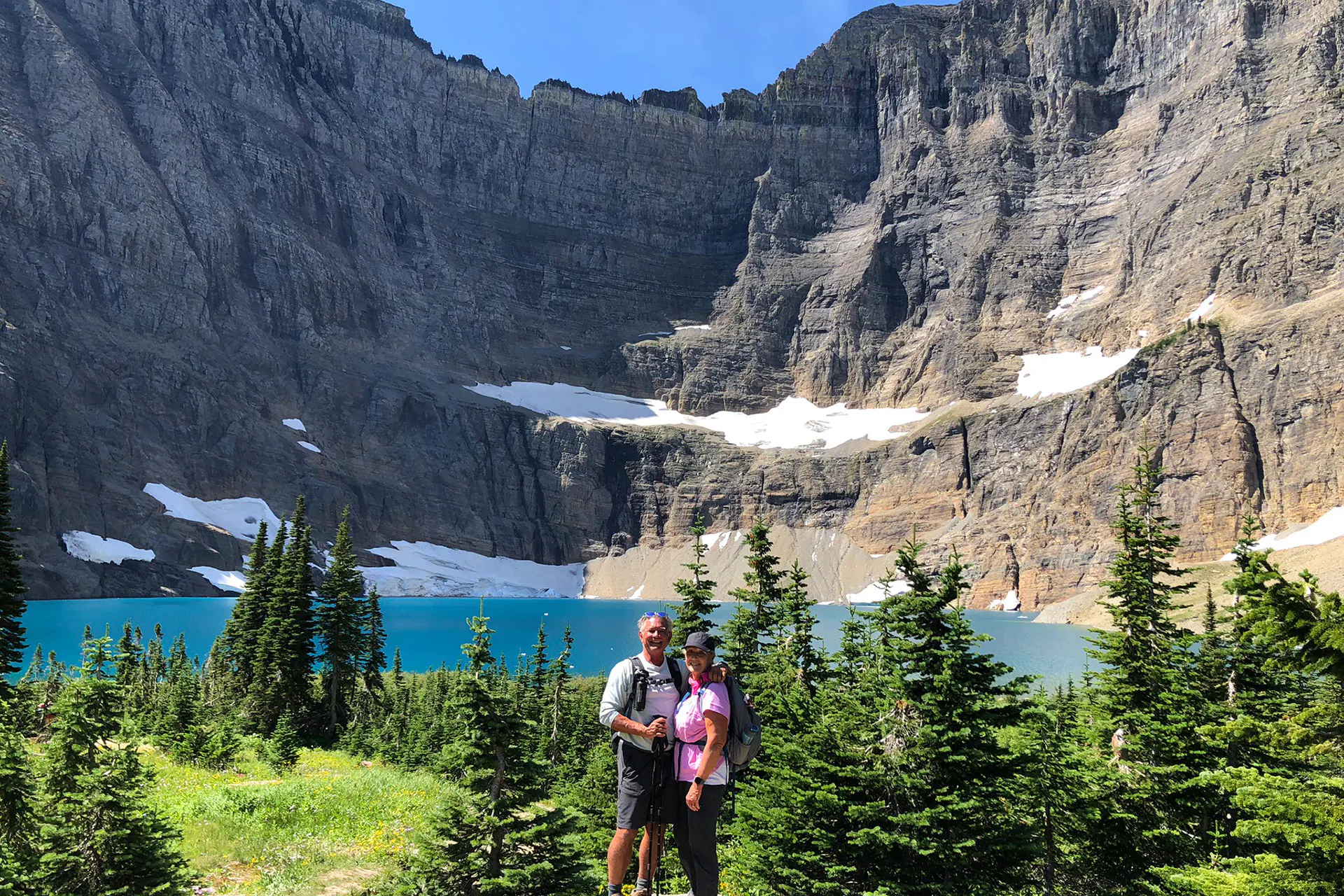 Couple standing in front of an alpine lake with snowfields behind in Glacier National Park, Montana