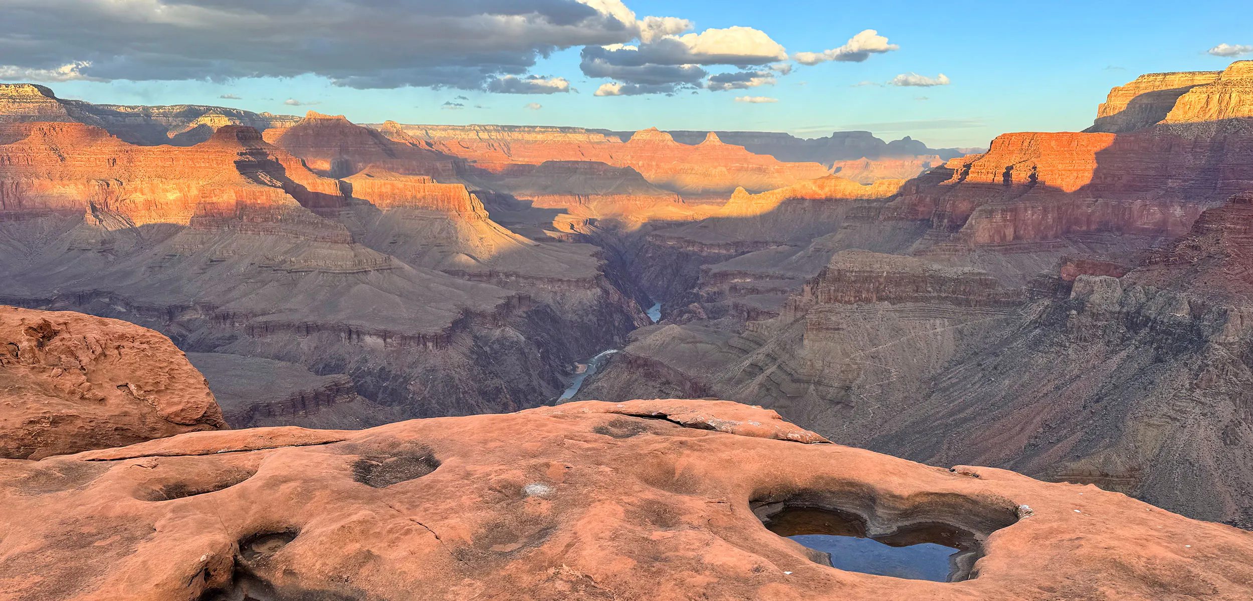 Yuma Point in Grand Canyon National Park with water-filled potholes in the foreground, and the Colorado River in the distance.