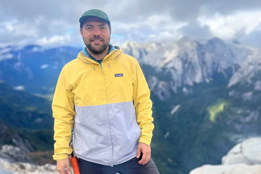 Jose Claro, one of the founders of Puelo Patagonia that saved the Cochamo Valley in Chile, standing in front of alpine peaks in a yellow Patagonia jacket