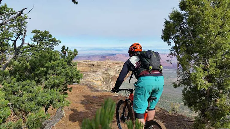 Mountain biker coasting through juniper and pine trees on a mesa over looking Utah deserts below