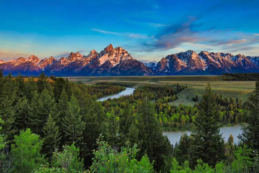 Red sunset light reflecting off the Tetons with the Snake River and forests in the foreground