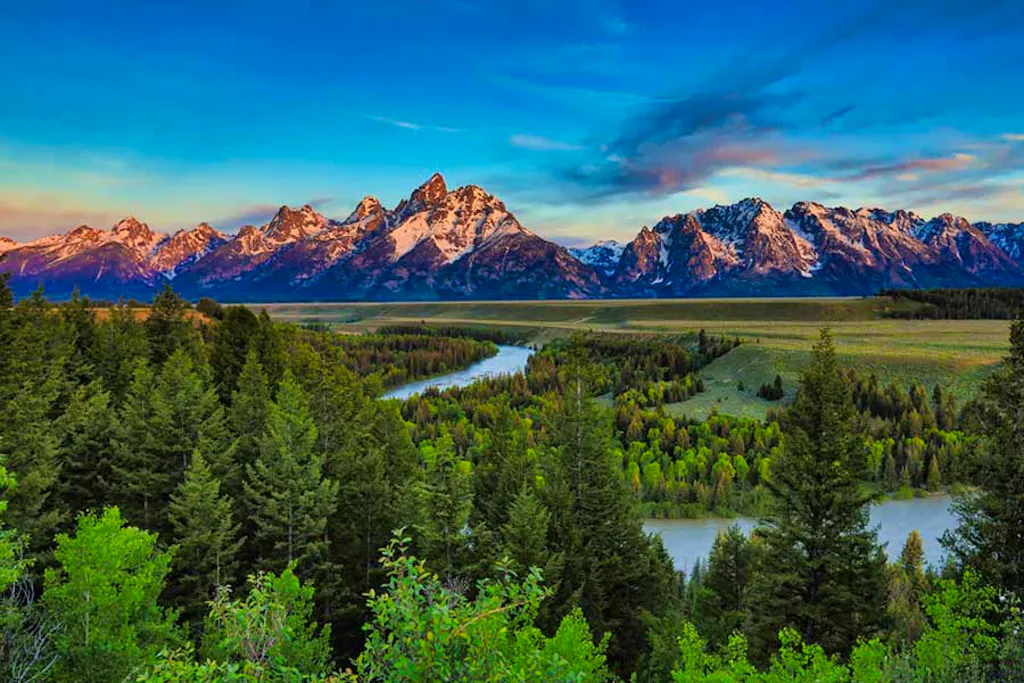 Red sunset light reflecting off the Tetons with the Snake River and forests in the foreground