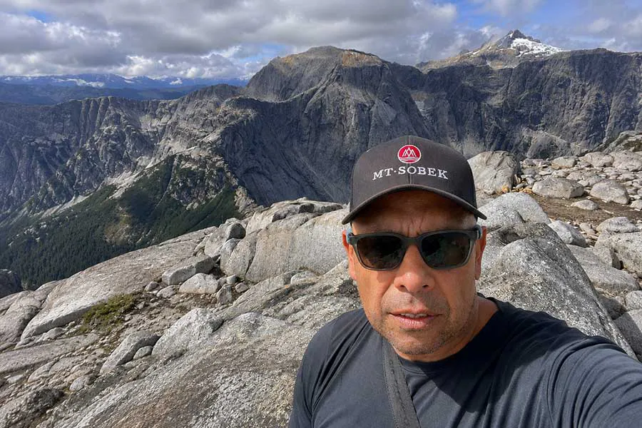 TC - MT Sobek's lead Patagonia guide for over four decades standing on a granite ridge with snowy peaks behind him