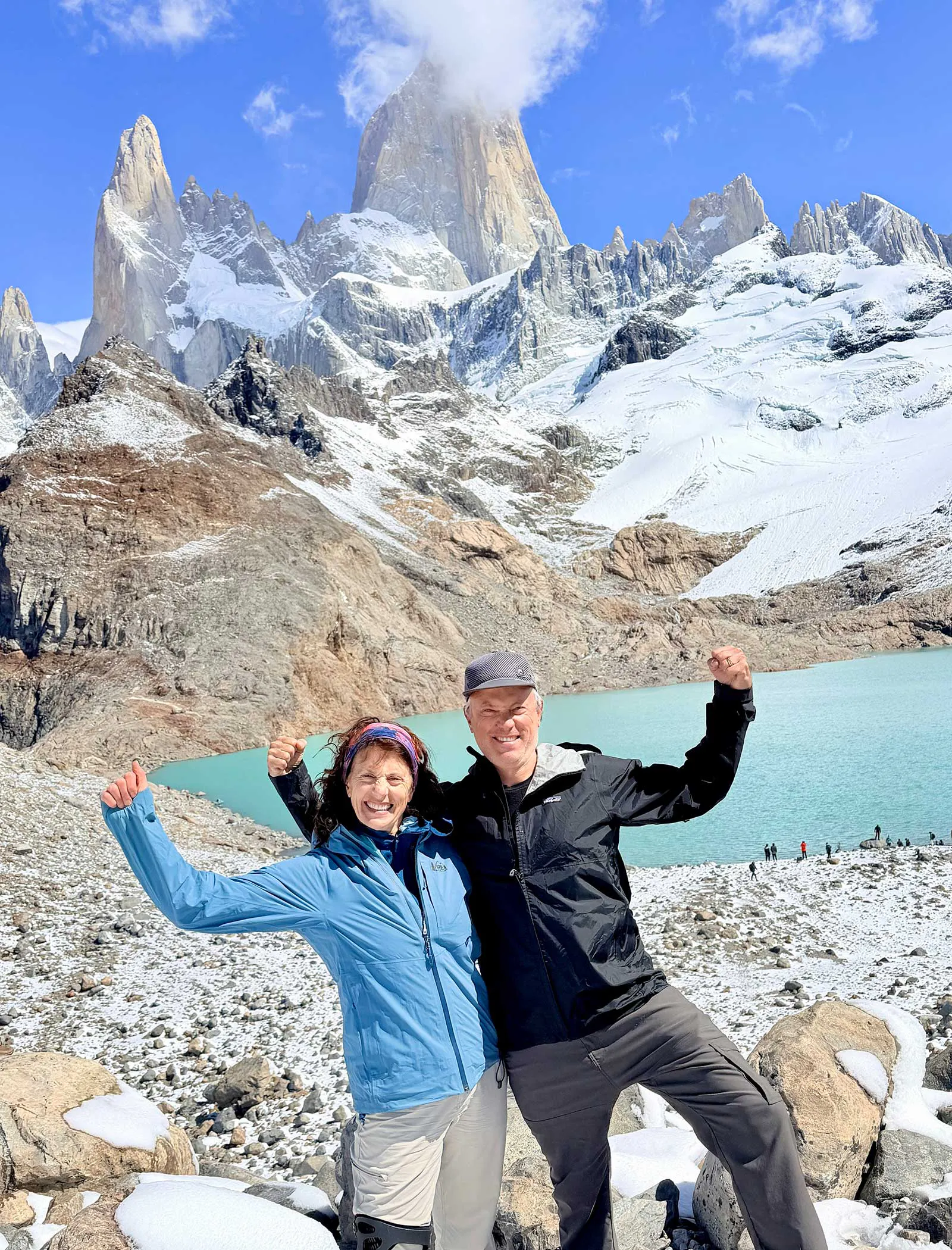 A couple in their 60s flexing muscles and smiling in front of an alpine lake and granite towers in Los Gaciares National Park in Argentina