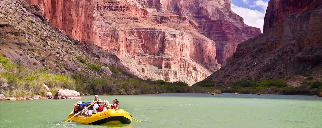 Rafts on the Colorado River with dramatic red cliffs in the backgrounds, OARS commercial Grand Canyon rafting expedition