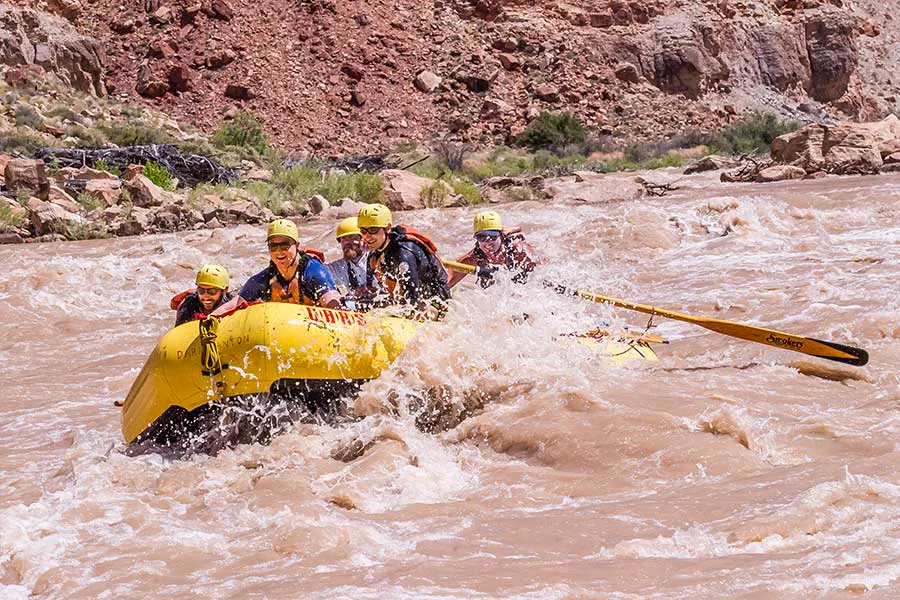 An OARS group crashing through a muddy rapid with big smiles in Cataract Canyon, Utah