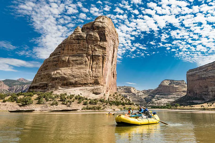 Two OARS rafts with guides and passengers on the Green River Gate of Lodore rafting expedition, massive sandstone buttress and wispy clouds