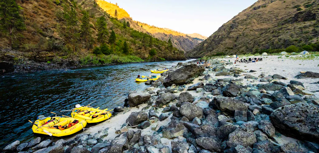 O.A.R.S rafting trip on the Lower Salmon River in Idaho—yellow rafts moored to a sandy shore and a camp with tents and passengers relaxing as the sun sets