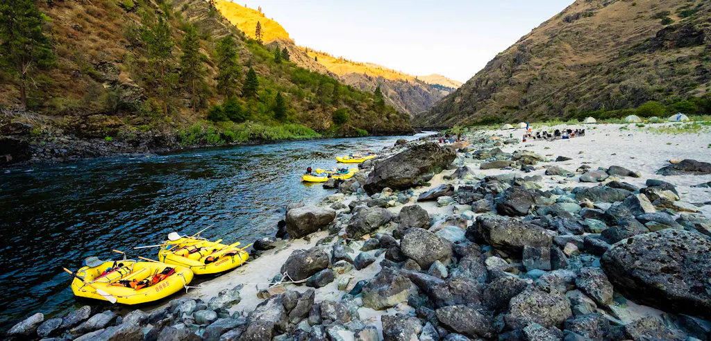 O.A.R.S rafting trip on the Lower Salmon River in Idaho—yellow rafts moored to a sandy shore and a camp with tents and passengers relaxing as the sun sets