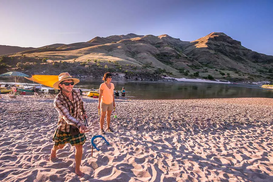 An OARS river guide and a guest on a sandy beach on the Lower Salmon River in Idaho laughing and playing horseshoes