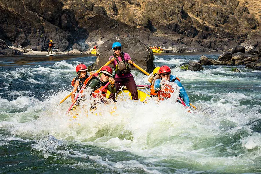 A group of OARS passengers crashing through a frothy rapid on the Lower Salmon River in Idaho—the guide is standing and the guests are smiling
