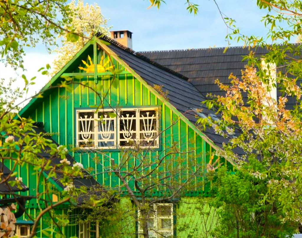 Casa cu Cerbi with dark roof tiles, surrounded by blooming trees and sunlight filtering through branches in spring—a perfect retreat after a day of hiking in Romania nearby.