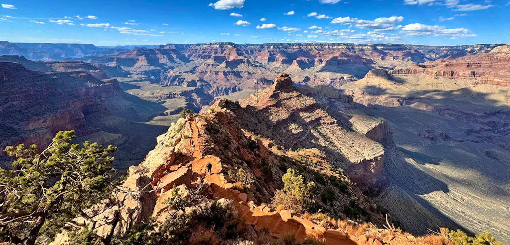 Enjoy a breathtaking view of the Grand Canyon’s layered rock formations, dramatic cliffs, deep valleys, and sparse vegetation under a blue sky with scattered clouds—an unforgettable sight often experienced on the best Phantom Ranch hiking tours. This classic scene captures the spirit of Grand Canyon hiking at its finest.