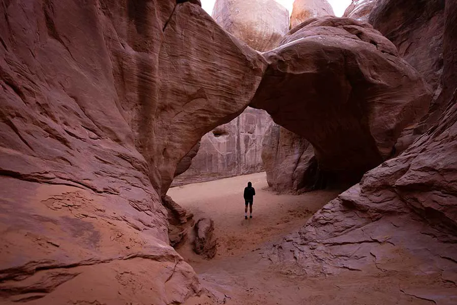 A man standing beneath Sand Dune Arch in Arches National Park, Utah